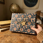 Mystical celestial wrapping paper with a vintage sun and moon pattern on a gift box, by Wrapped Studios.
