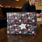 Navy blue Christmas wrapping paper with red ornaments on a gift box with a star tag, by Wrapped Studios.