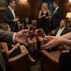 Luxury gift wrap in a brown wood pattern with a velvet bow, passed at an elegant party by Wrapped Studios.