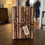 Cigar wrapping paper with a brown leather bow and Wrapped Studios tag on a rustic wooden table.