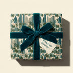 Luxury cityscape wrapping paper with a teal velvet bow and gift tag by Wrapped Studios.