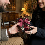 Luxury dark floral wrapping paper with a burgundy satin bow on a gift held by a couple. Wrapped Studios.