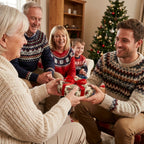 Family exchanging gift in botanical Christmas wrapping paper with red bow by Wrapped Studios.