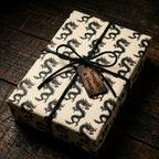 Cream dragon wrapping paper with a black leather bow and wooden tag, luxury gift wrap by Wrapped Studios.