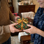 Couple exchanging a gift in retro green Christmas wrapping paper with a gold bow, by Wrapped Studios.