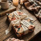 Vintage floral wrapping paper with a cream silk ribbon bow on a rustic wooden table by Wrapped Studios.