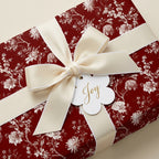 Red floral wrapping paper with cream bow and 'Joy' tag for luxury holiday gift wrap by Wrapped Studios.