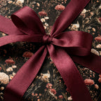 Vintage moody floral wrapping paper with a burgundy satin bow. Elegant gift wrap by Wrapped Studios.