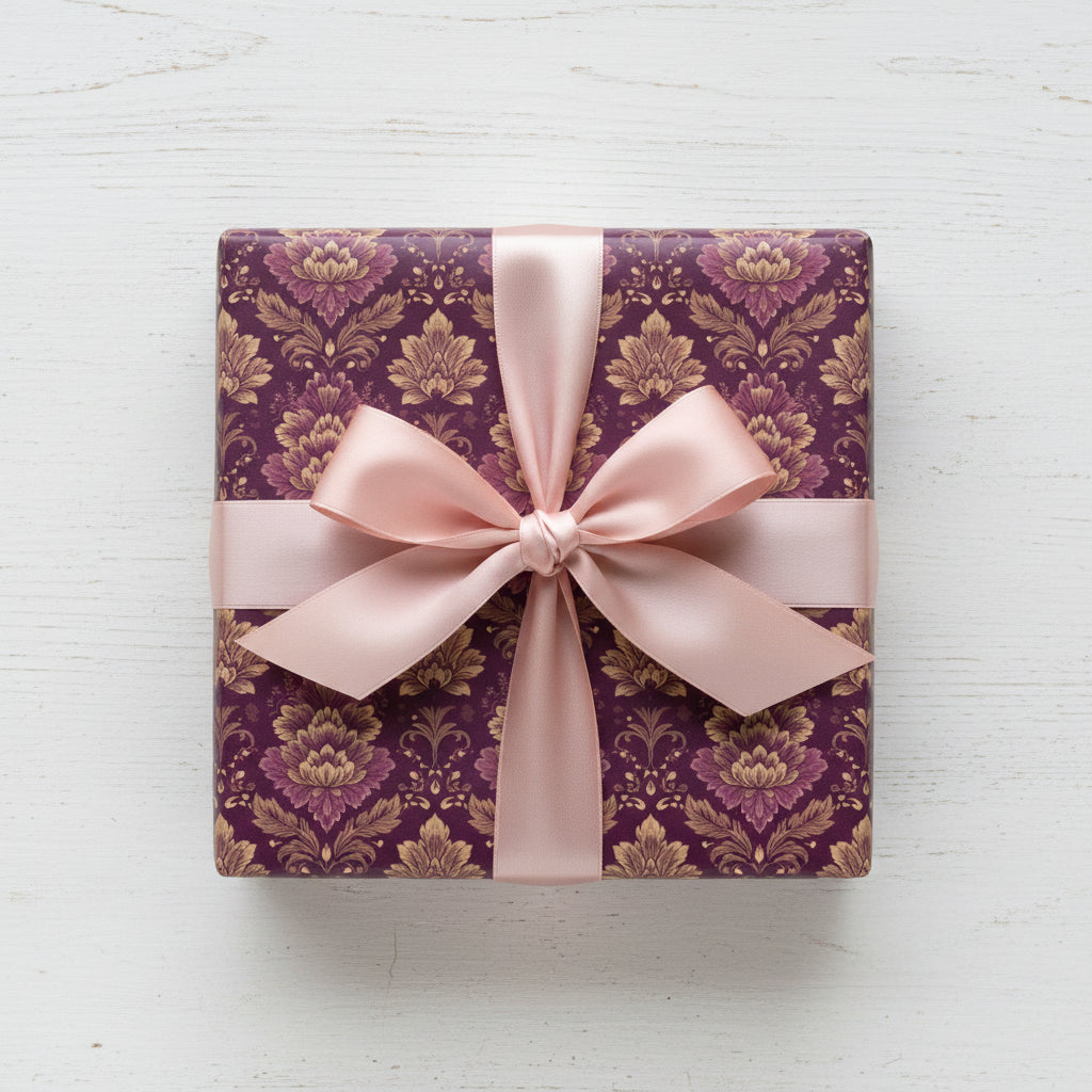 Elegant square gift wrapped in purple floral wrapping paper with light pink ribbon bow on a white wood surface.