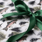 Fly fishing gift wrap featuring trout and lures with a green satin bow. Rustic wrapping paper by Wrapped Studios.