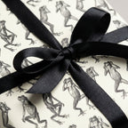 Gift wrapped in off-white paper with leaping frog drawings and tied with a black satin ribbon.