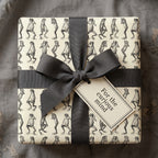 Square gift wrapped in frog-patterned paper with a gray ribbon and a tag that says "For the curious mind".