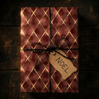 Luxury burgundy and gold Christmas wrapping paper with a Noel tag on rustic wood, by Wrapped Studios.