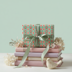 Mint green and coral mid-century modern pattern gift wrap with sage ribbon on a stack of pastel books and dried flowers.
