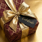 Luxury burgundy and gold gift wrap with a metallic bow and "Celebrate" tag by Wrapped Studios.