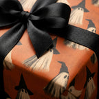 Ghost Halloween wrapping paper in orange with a black satin bow on a gift box, by Wrapped Studios.