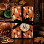 Spooky orange ghost Halloween wrapping paper with a black velvet ribbon by Wrapped Studios.