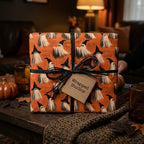 Orange Halloween wrapping paper with a spooky ghost pattern and black ribbon by Wrapped Studios.
