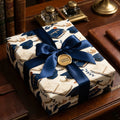 Elegant graduation wrapping paper with books and caps, tied with a navy satin bow by Wrapped Studios.