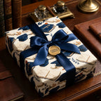 Elegant graduation wrapping paper with books and caps, tied with a navy satin bow by Wrapped Studios.