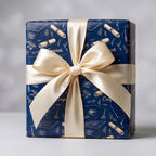 Navy graduation wrapping paper with gold caps, diplomas, and a cream bow by Wrapped Studios.