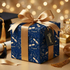 Navy blue graduation wrapping paper with gold caps, diplomas, and a satin bow, by Wrapped Studios.