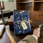 Navy blue graduation gift wrap with gold caps and twine bow on a study desk by Wrapped Studios.