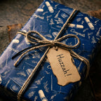 Graduation wrapping paper in navy blue with a congrats pattern, tied with rustic twine by Wrapped Studios.