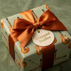 Vintage electric guitar wrapping paper on a gift box with copper ribbon and a Wrapped Studios tag.