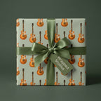 Guitar wrapping paper with electric guitars on sage green, with a satin green bow by Wrapped Studios.