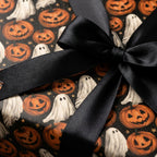 Halloween wrapping paper with ghosts and pumpkins, tied with a black satin bow by Wrapped Studios.