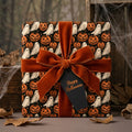 Halloween wrapping paper with ghosts and pumpkins, tied with an orange velvet ribbon by Wrapped Studios.