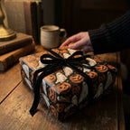 Vintage Halloween wrapping paper with ghosts and pumpkins on a gift box with black ribbon by Wrapped Studios.
