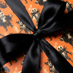 Spooky orange Halloween wrapping paper with skeleton pattern and black satin bow by Wrapped Studios.