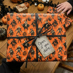 Spooky vintage Halloween wrapping paper with orange monster pattern and black ribbon by Wrapped Studios.