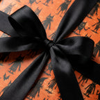 Spooky Halloween wrapping paper with black cats on orange, tied with a black satin bow. Wrapped Studios.