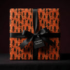 Spooky Halloween wrapping paper with black monsters on orange, tied with a black bow by Wrapped Studios.