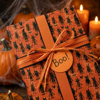 Spooky Halloween wrapping paper with black monsters, raffia bow, and "Boo!" tag by Wrapped Studios.