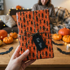 Spooky orange Halloween wrapping paper with black monsters and a twine bow, from Wrapped Studios.