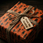 Spooky Halloween wrapping paper with cute black goblins on orange, tied with twine by Wrapped Studios.