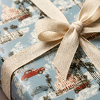 Retro travel wrapping paper with classic cars and palm trees, tied in a cream linen bow by Wrapped Studios.