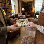 Exchanging a gift wrapped in unique insect-themed wrapping paper, tied with black string in a vintage library setting.