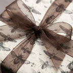 Elegant gift wrapped in insect pattern wrapping paper with sheer brown bow.