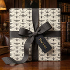 Elegant gift wrapped in insect pattern wrapping paper with gray ribbon, "For You" tag, sitting on a wooden table with books in the background.