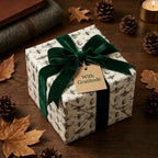Elegant gift wrapped in insect-patterned paper with velvet green ribbon and "With Gratitude" tag.