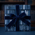Book lover gift wrap with a vintage library bookshelf pattern and navy velvet bow, by Wrapped Studios.