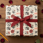 Vintage love-themed wrapping paper with red roses, birds, and "LOVE" text, tied with a deep red satin ribbon on a rustic wooden table with scattered rose petals.
