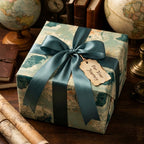 Vintage map wrapping paper with a teal satin bow on a travel-themed gift box by Wrapped Studios.