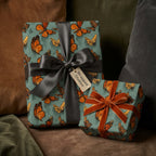 Gifts wrapped in teal butterfly wrapping paper with grey and rust velvet ribbon, against a textured backdrop.