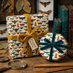 Vintage-inspired wrapping paper featuring colorful moth illustrations, adorned with mustard twine and a teal velvet ribbon bow.
